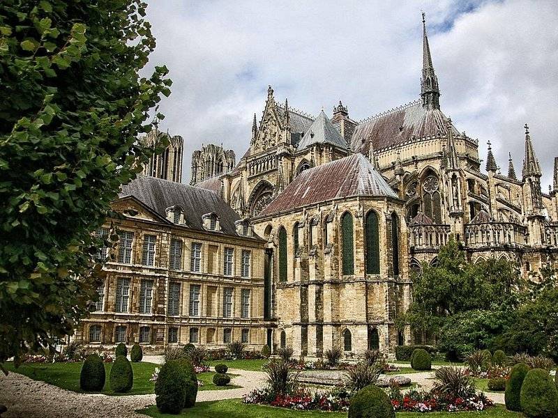 The east end of Reims Cathedral rising behind a formal garden and an older building
