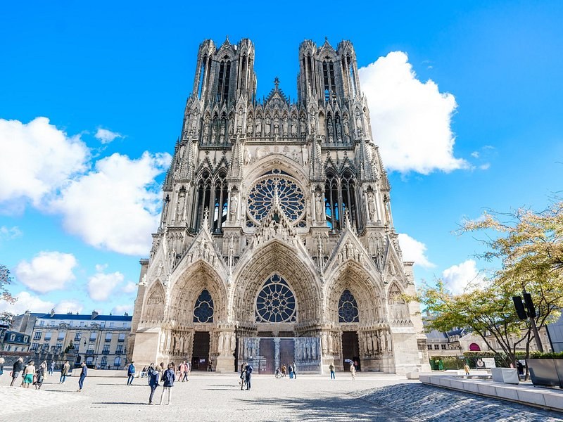 Reims Cathedral's west front and its two towers under a blue sky with white cloud